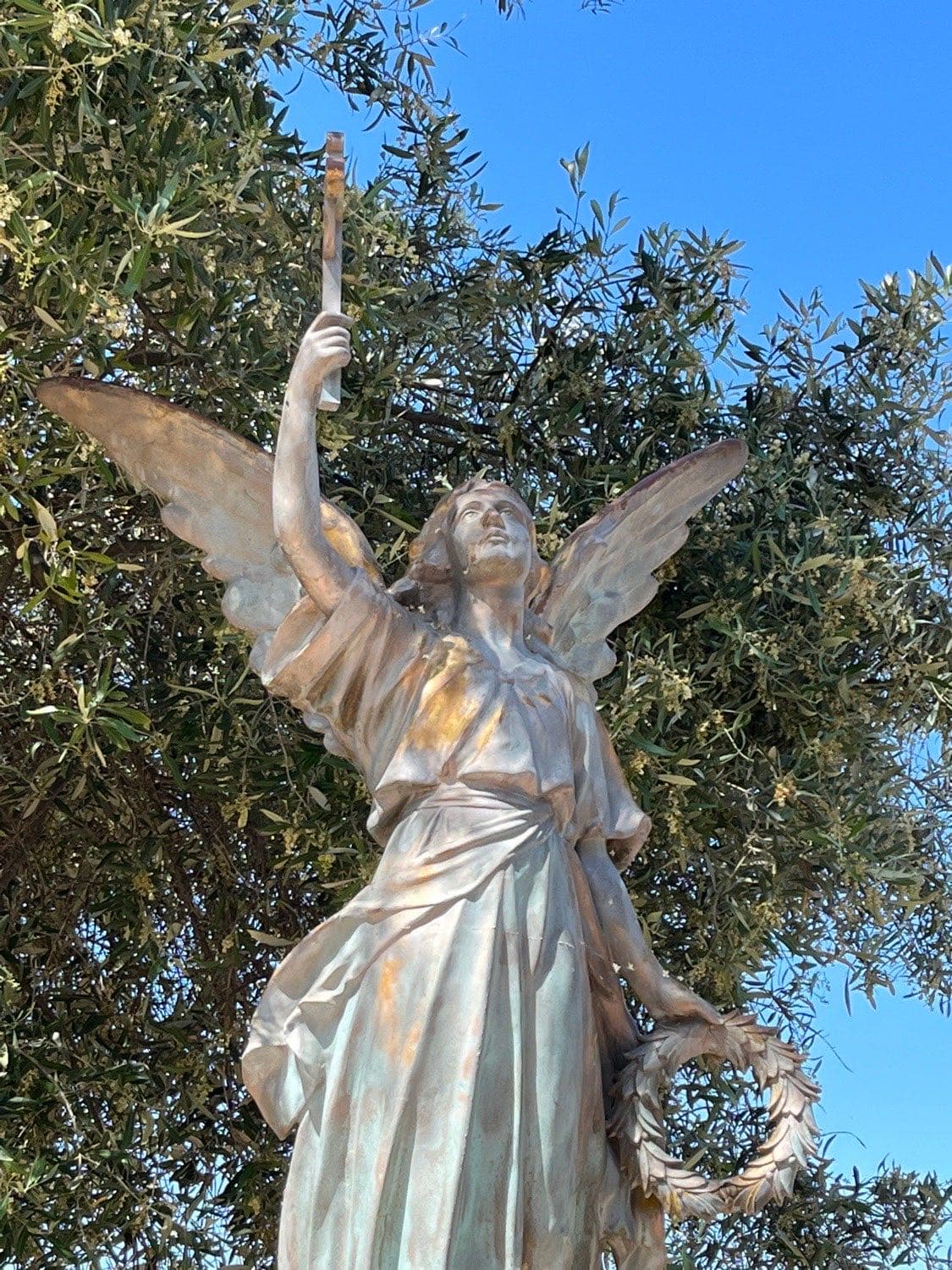 A bronze angel statue on the church grounds, holding a torch and a crown